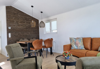 Soggiorno moderno nello Chalet Alme con divano marrone, zona pranzo, poltrone verdi e cuscini decorativi.
