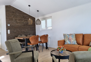 Modernes Wohnzimmer im Chalet Alme mit braunem Sofa, Esstisch, grünen Sesseln und Deko-Kissen.