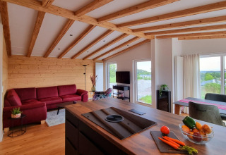 Modern chaletinterieur met zichtbare houten balken, rode sofa en grote ramen in Brilon, Duitsland.