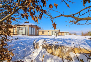 Chalet Enzian en Camping & Ferienpark Brilon, Alemania, rodeado de nieve y ramas secas bajo un cielo azul claro.