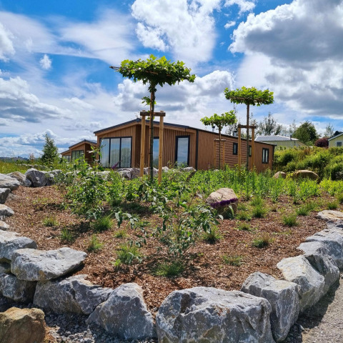 Cabaña de madera Chalet Enzian en Camping & Ferienpark Brilon, Alemania, rodeada de plantas y rocas.