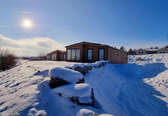 Zonnige winterdag bij Chalet Enzian, Camping & Ferienpark Brilon in Duitsland, omgeven door sneeuw en hutten.
