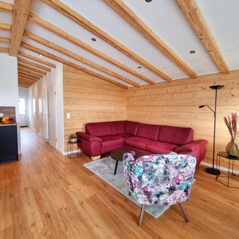 Sala en Chalet Enzian con paredes de madera, vigas, sofá rojo y silla floral en Camping & Ferienpark Brilon, Alemania.