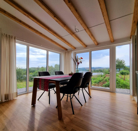 Luminoso comedor en Chalet Enzian con grandes ventanales y vistas al paisaje campestre en Brilon, Alemania.