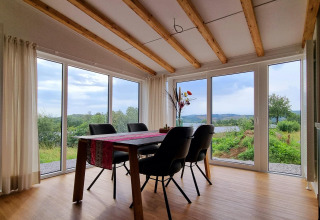 Luminoso comedor en Chalet Enzian con grandes ventanales y vistas al paisaje campestre en Brilon, Alemania.