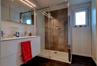 Baño moderno con ducha, tocador blanco y espejo en Chalet Enzian, Camping & Ferienpark Brilon, Alemania.