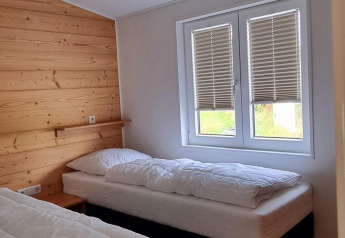 Sfeervolle slaapkamer in Chalet Enzian met twee eenpersoonsbedden, houten wand en raam met jaloezieën.