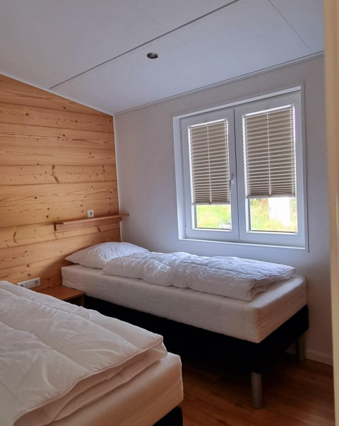 Agradable dormitorio en Chalet Enzian con dos camas individuales, pared de madera y ventana con persianas.