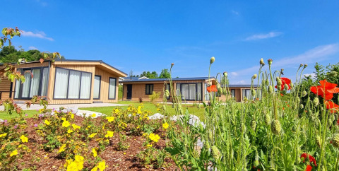 Chalet Enzian en Camping & Ferienpark Brilon, Alemania, rodeado de flores y cielo azul brillante.