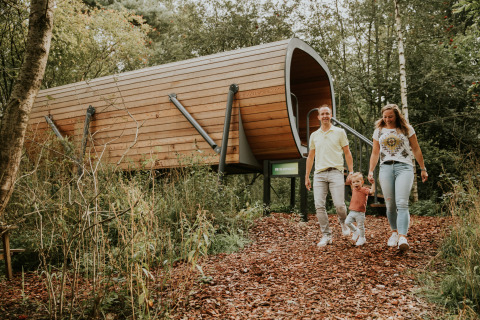 Family outside Skycabin, a nature house at Camping Si-Es-An in the Netherlands, surrounded by woods.