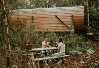 Una pareja disfruta de un picnic en una mesa de madera frente a una Skycabin en Camping Si-Es-An, Países Bajos.