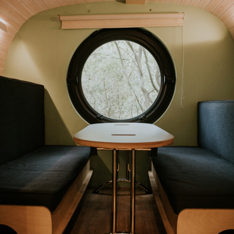 Interior de Skycabin en Camping Si-Es-An, Países Bajos, con ventana circular y acogedor comedor.