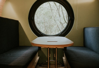 Interior de Skycabin en Camping Si-Es-An, Países Bajos, con ventana circular y acogedor comedor.