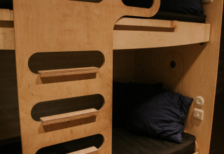 Litera moderna de madera con ropa de cama oscura, en Skycabin, Nature house, Camping Si-Es-An, Países Bajos.
