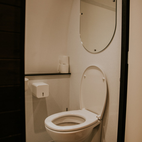 Baño moderno con inodoro blanco, espejo y papel higiénico en la Skycabin de Camping Si-Es-An, Países Bajos.