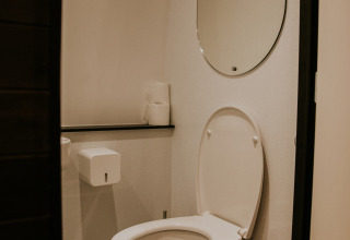 Baño moderno con inodoro blanco, espejo y papel higiénico en la Skycabin de Camping Si-Es-An, Países Bajos.