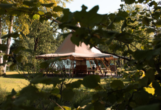A glamping tent viewed through greenery at Skycabin, Nature house at Camping Si-Es-An in the Netherlands.