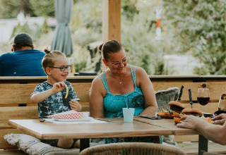 A happy family enjoys an outdoor meal at Skycabin, a nature house at Camping Si-Es-An in the Netherlands.