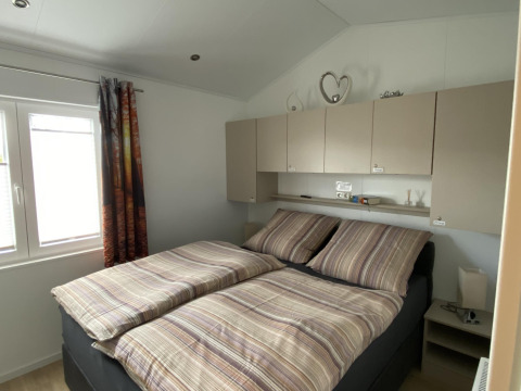 Dormitorio con cama doble, ropa de cama a rayas, armarios superiores y ventana en Chalet Waldfee, Alemania.