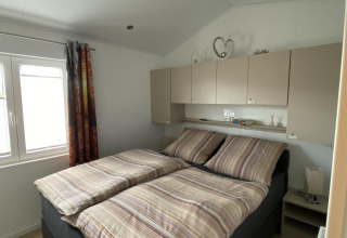 Dormitorio con cama doble, ropa de cama a rayas, armarios superiores y ventana en Chalet Waldfee, Alemania.