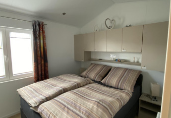 Dormitorio con cama doble, ropa de cama a rayas, armarios superiores y ventana en Chalet Waldfee, Alemania.