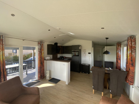 Acogedora sala y cocina en el Chalet Waldfee de Camping & Ferienpark Brilon, Alemania, con cortinas de bosque.