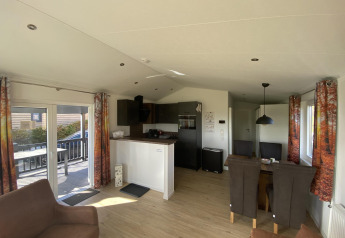 Acogedora sala y cocina en el Chalet Waldfee de Camping & Ferienpark Brilon, Alemania, con cortinas de bosque.