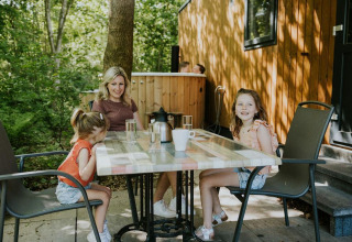 Een gezin aan een buitentafel bij Happy bee lodge, Camping Si-Es-An in Nederland, te midden van het groen.
