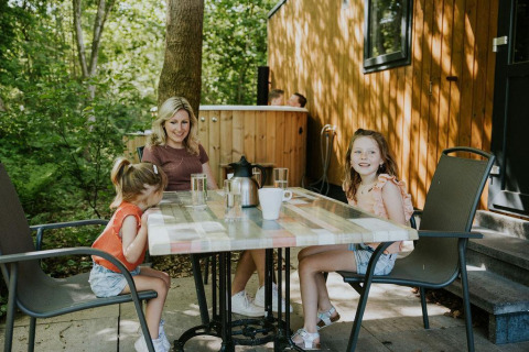 Une famille assise à une table en plein air à Happy bee lodge, Camping Si-Es-An, aux Pays-Bas, entourée de nature.