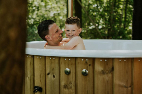 Un padre y su hijo disfrutan juntos de un jacuzzi exterior en Happy bee lodge, Camping Si-Es-An, Países Bajos.