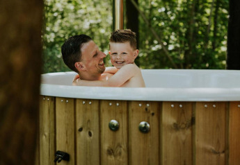 Padre e figlio si rilassano in una vasca idromassaggio all'aperto a Happy bee lodge, Camping Si-Es-An, Olanda.
