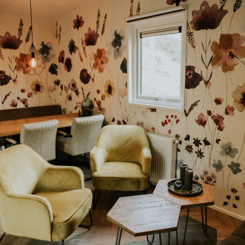 Acogedora zona de asientos en Happy Bee Lodge, Camping Si-Es-An, Países Bajos, con papel floral y sillas modernas.