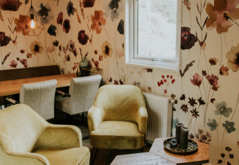 Zona salotto accogliente alla Happy Bee Lodge, Camping Si-Es-An, Paesi Bassi, con carta da parati floreale e sedie moderne.