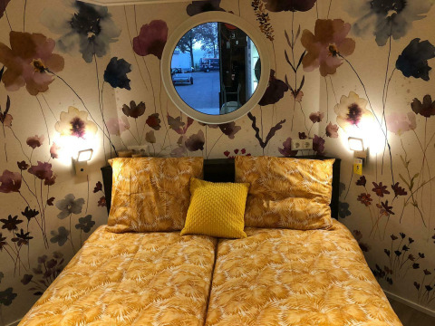 Dormitorio en Happy bee lodge, Camping Si-Es-An, Países Bajos, con ropa de cama amarilla y papel pintado floral.