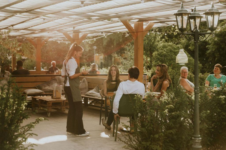 Área de cafetería al aire libre en Happy bee lodge, Camping Si-Es-An, Países Bajos, con clientes y camarera.