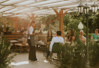 Área de cafetería al aire libre en Happy bee lodge, Camping Si-Es-An, Países Bajos, con clientes y camarera.