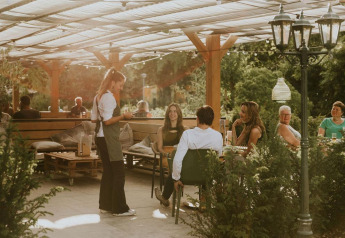 Área de cafetería al aire libre en Happy bee lodge, Camping Si-Es-An, Países Bajos, con clientes y camarera.