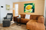 Sala de estar en Chalet Bergrose, Camping & Ferienpark Brilon, Alemania, con sofá marrón y arte floral.