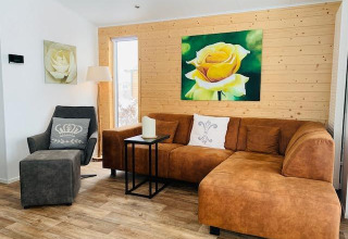 Sala de estar en Chalet Bergrose, Camping & Ferienpark Brilon, Alemania, con sofá marrón y arte floral.