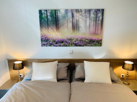 Dormitorio acogedor en Chalet Bergrose con cama doble, mesitas y cuadro de bosque en Camping & Ferienpark Brilon.