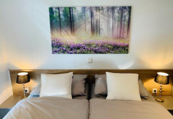 Dormitorio acogedor en Chalet Bergrose con cama doble, mesitas y cuadro de bosque en Camping & Ferienpark Brilon.