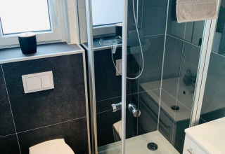 Baño moderno y compacto con ducha, inodoro y ventana en Chalet Bergrose de Camping & Ferienpark Brilon, Alemania.