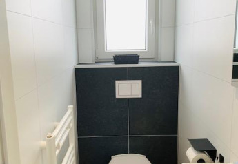 Baño moderno blanco con inodoro suspendido, ventana pequeña y lavabo en Chalet Bergrose, Alemania.