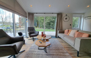 Salón moderno en la cabaña Hackfort 4 en De Utrechtse Heuvelrug, Países Bajos, con muebles elegantes y ventana grande.