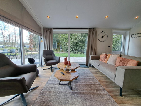 Salón moderno en la cabaña Hackfort 4 en De Utrechtse Heuvelrug, Países Bajos, con muebles elegantes y ventana grande.