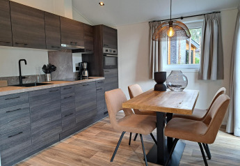 Cucina moderna e zona pranzo con tavolo di legno e quattro sedie nella lodge Hackfort 4 a De Utrechtse Heuvelrug.