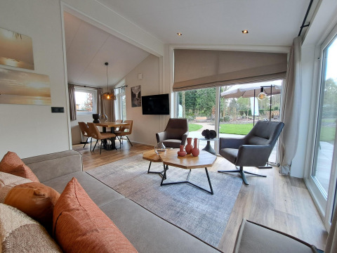 Sala moderna de la cabaña Hackfort 4 con grandes ventanales y vista al jardín, De Utrechtse Heuvelrug, Países Bajos.