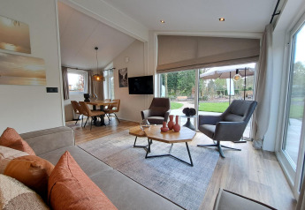 Salon moderne du lodge Hackfort 4 avec grandes baies vitrées et vue sur jardin à De Utrechtse Heuvelrug, Pays-Bas.