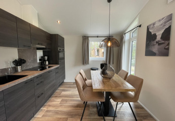 Modern kitchen and dining area in Hackfort 4 lodge at De Utrechtse Heuvelrug, Netherlands, with wooden table.