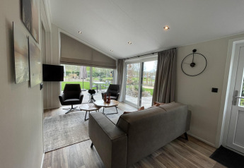 Soggiorno moderno nella lodge Hackfort 4 a De Utrechtse Heuvelrug, Paesi Bassi, con grandi finestre e arredi moderni.